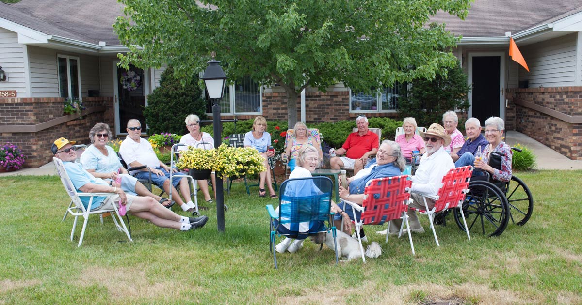 Group of seniors socializing on lawn in front of their retirement residence